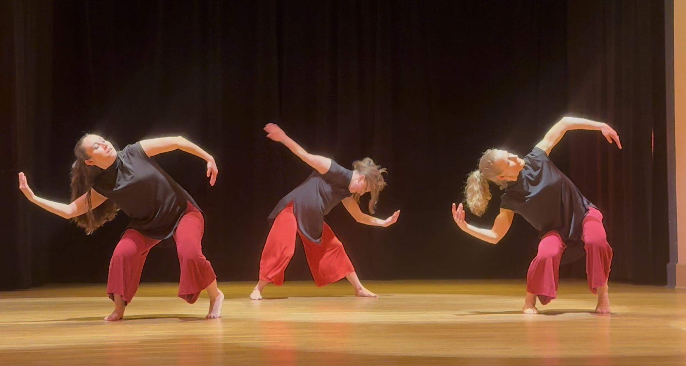 three modern dancers on stage in loose red pants and black tops